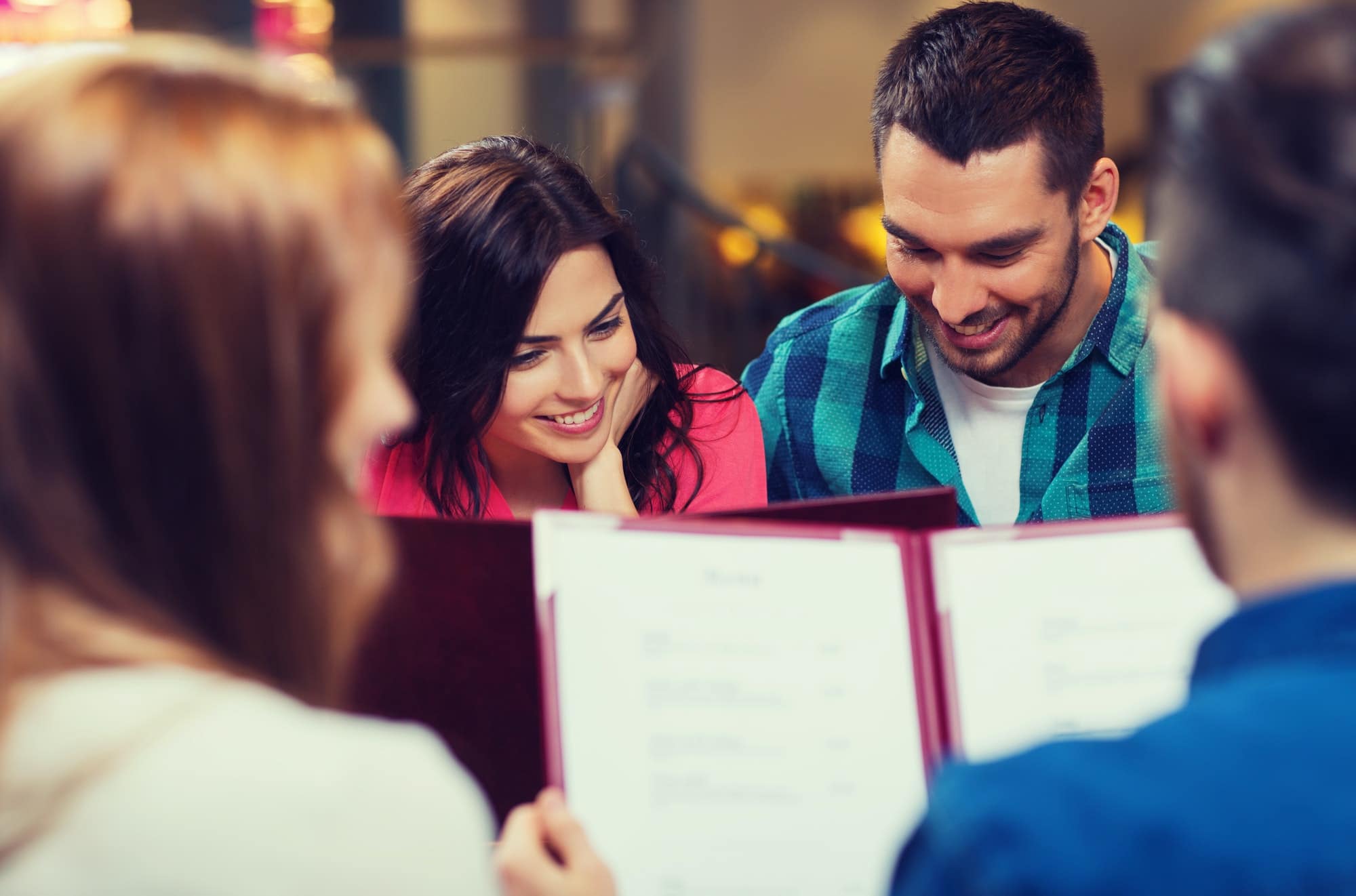 smiling couple with friends and menu at restaurant
